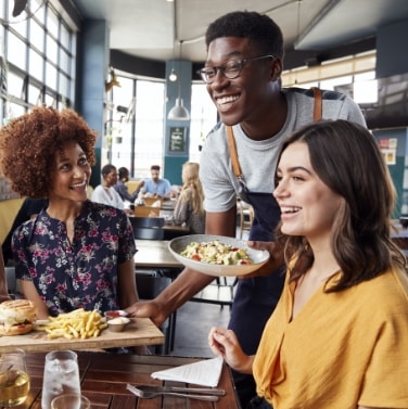 man serving food to two women, all smiling, in a restaurant